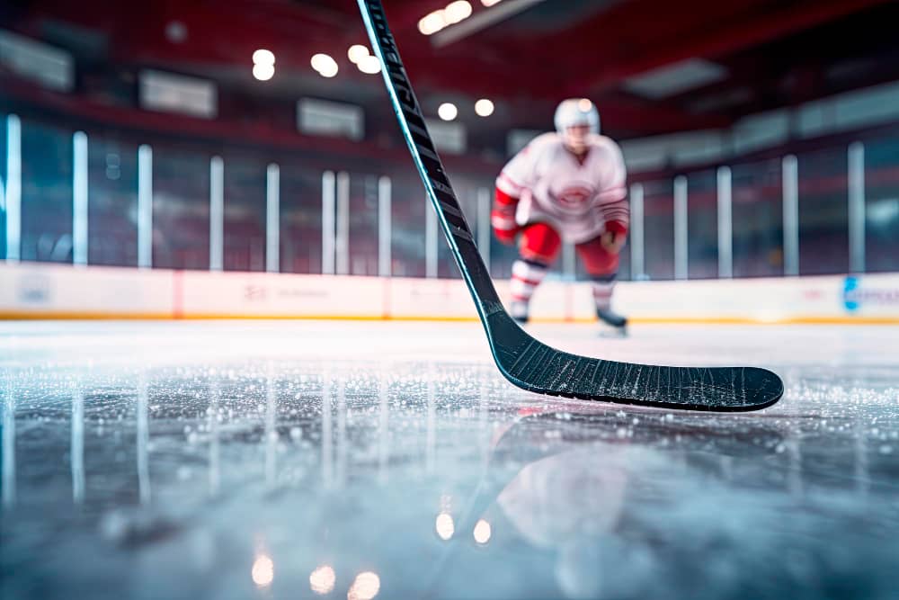 Close-up of an ice hockey stick on the rink, player in the background, ready for a thrilling NHL match.